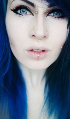  Piercing bridge et multiples autres piercings dorés sur femme aux cheveux bleus 