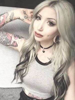  Piercing cheek, joue, fossette sur femme avec des tatouages au bras et un plug à l’oreille 