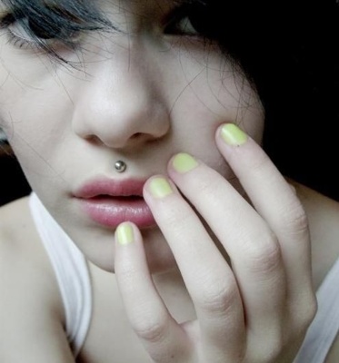  Piercing medusa simple boule sur femme avec des ongles jaunes