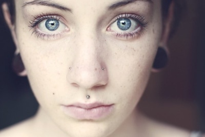  Piercing medusa sur femme aux yeux bleu qui porte aussi deux gros plugs aux oreilles 