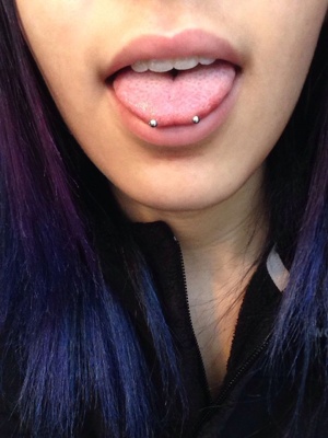  Piercing langue snake eyes sur femme aux cheveux violets.